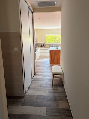A narrow hallway with a wooden bench, a kitchen area with a window, and a sliding door.