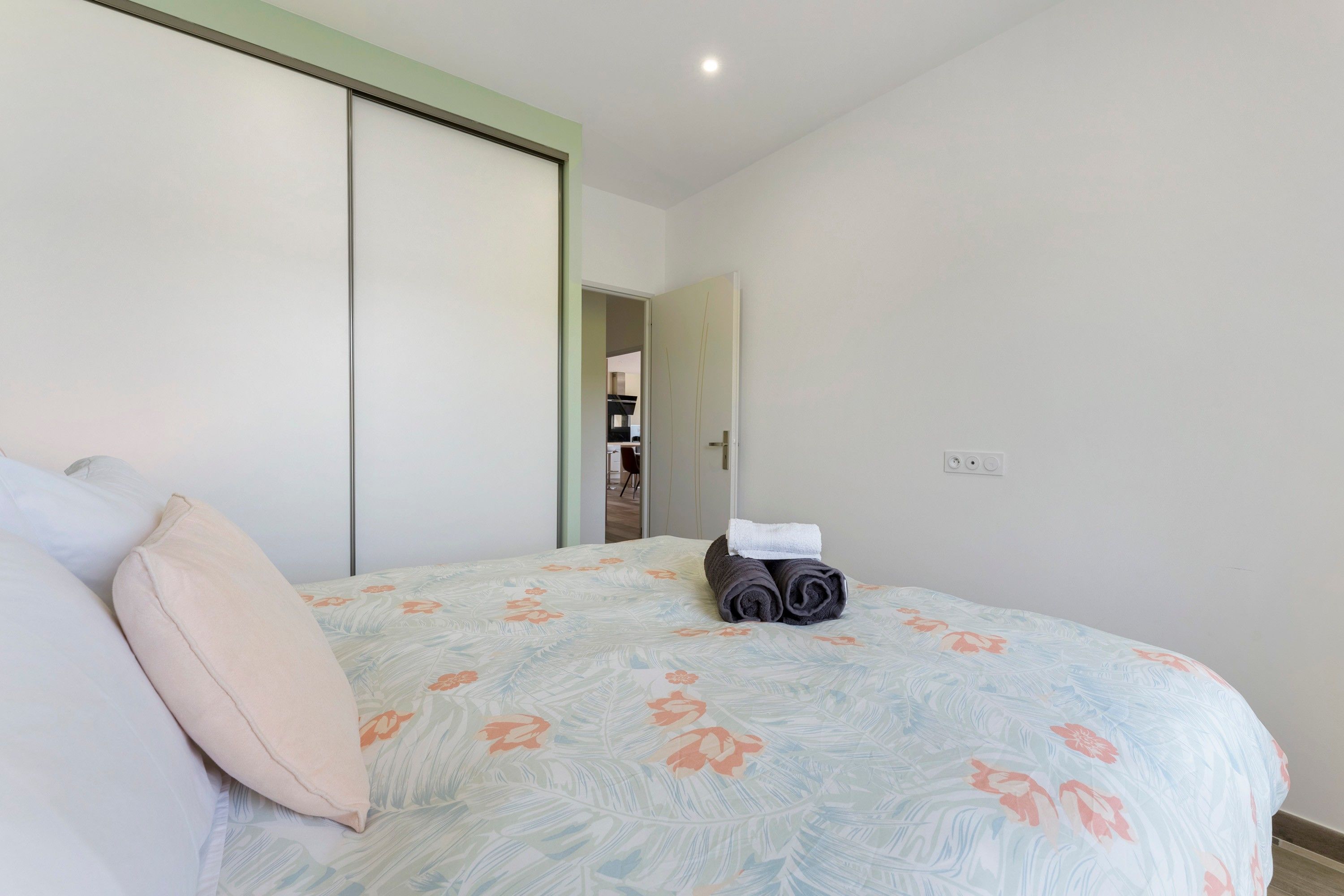 Une chambre à coucher avec un lit, des oreillers, une serviette enroulée et une porte donnant sur une salle de bain.