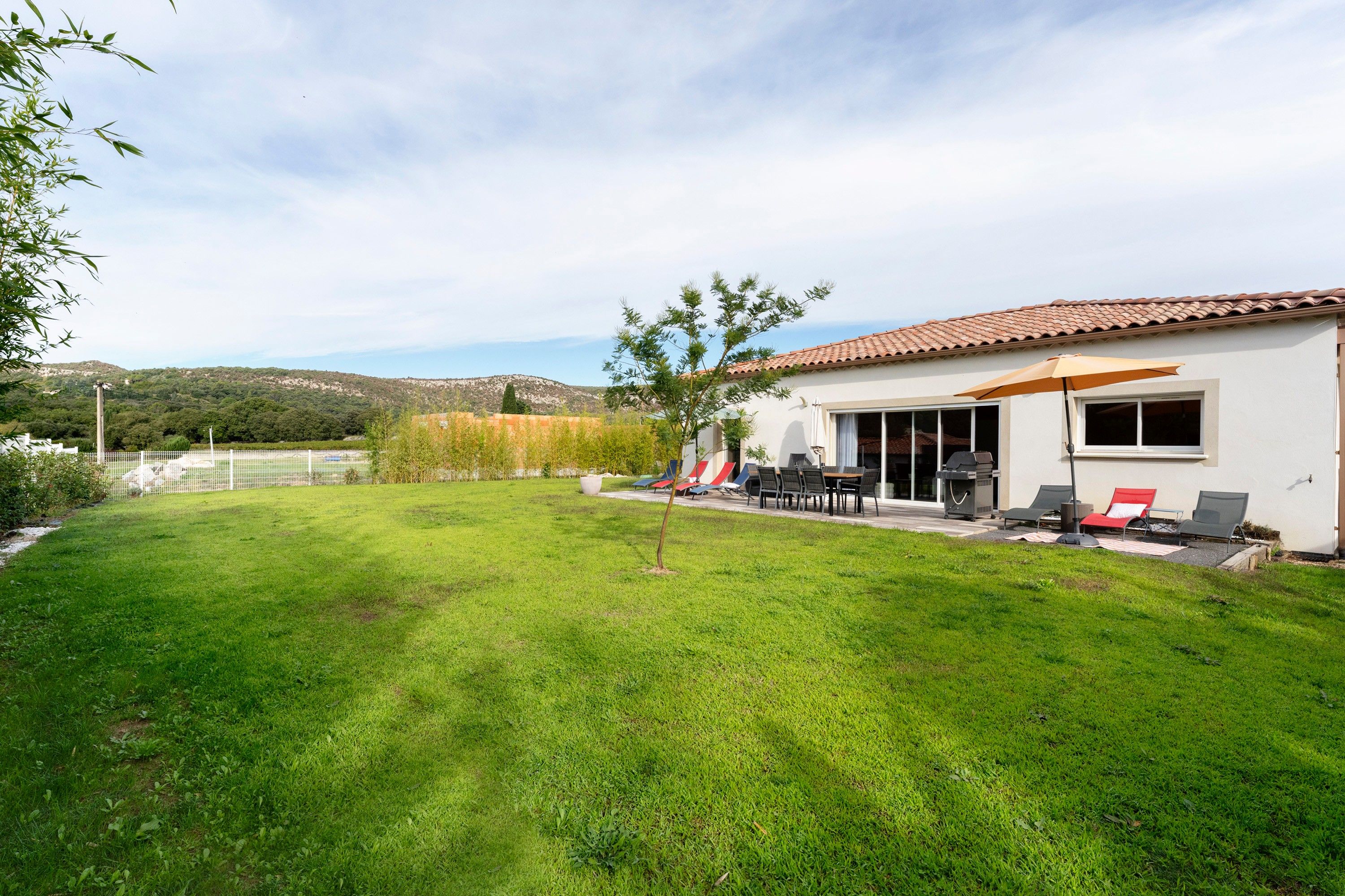 Une maison moderne dotée d’un patio, de mobilier d’extérieur et offrant une vue sur un paysage vallonné.