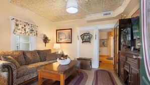 A living room with a patterned sofa, a wooden coffee table, and a decorative lamp. There is a framed picture on the wall and a cabinet with glass doors. - Queen Anne Victorian home plus private Cottage in pleasant Dennisport Cape Cod (Dennis)