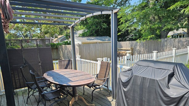 An outdoor patio with a round table and chairs, a pergola, and a covered grill area. - Queen Anne Victorian home plus private Cottage in pleasant Dennisport Cape Cod (Dennis)