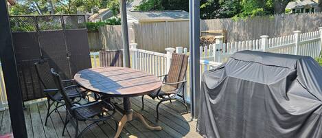 Une terrasse extérieure avec une table ronde et des chaises, une pergola et un espace barbecue couvert.