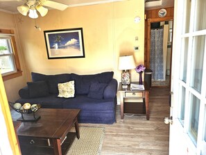 Ein Wohnzimmer mit einem blauen Sofa, einem Couchtisch, einem gerahmten Bild, einer Lampe und einem kleinen Tisch mit einer Dekorationsgegenstand.