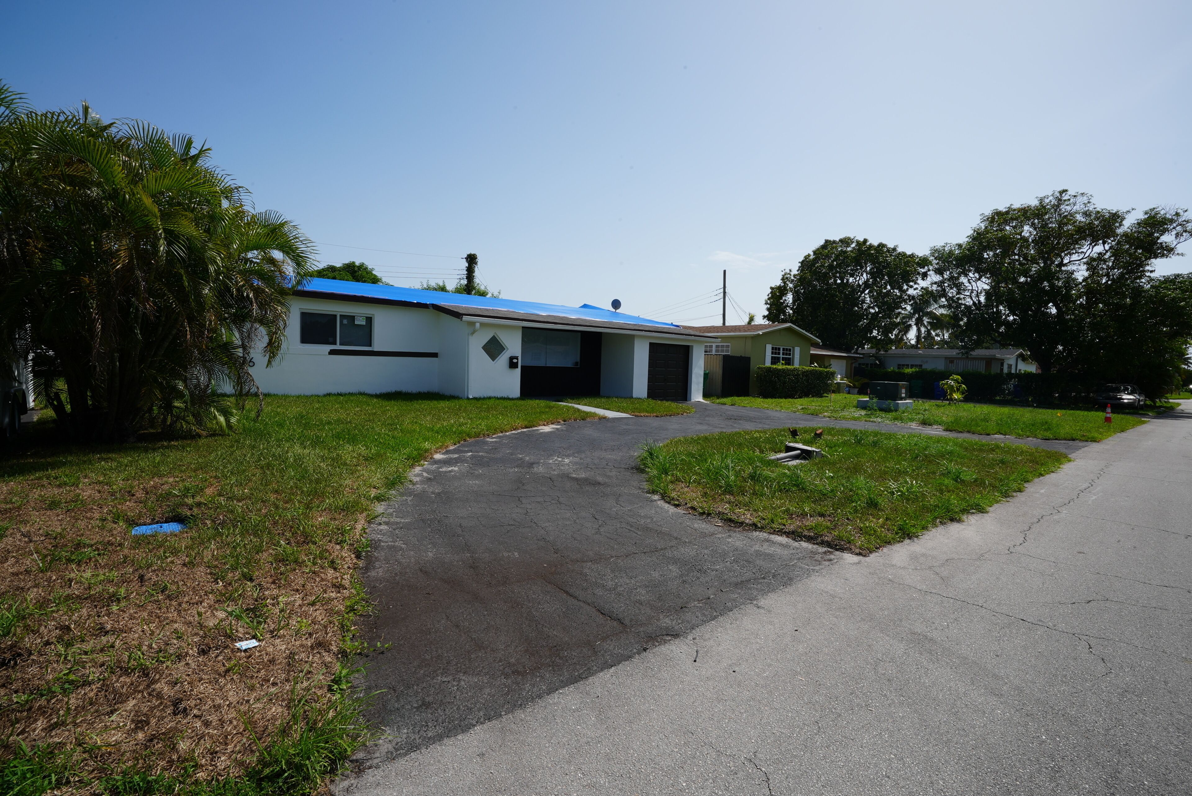A single-story house with a blue roof, a driveway leading to the garage, and a well-maintained lawn.