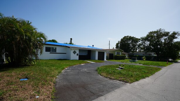 A single-story house with a blue roof, a driveway leading to the garage, and a well-maintained lawn.