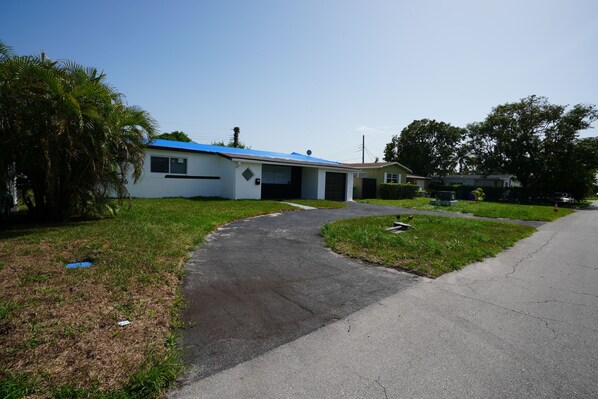 A single-story house with a blue roof, a driveway leading to the garage, and a well-maintained lawn.