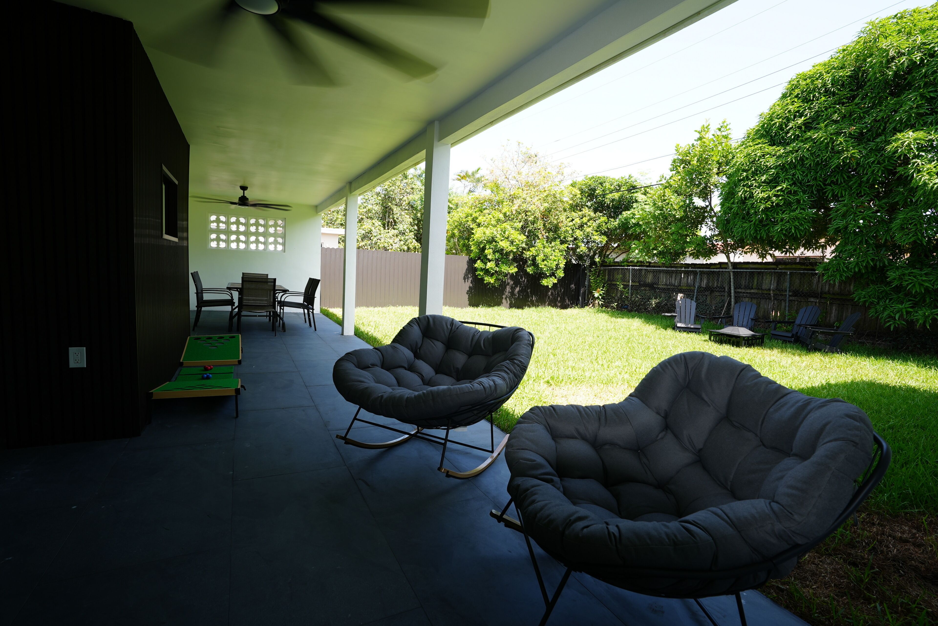 A covered patio with two rocking chairs, a table, and a green pool table.