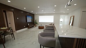 A modern living room with a marble floor, a sofa set, a TV, and a large window.