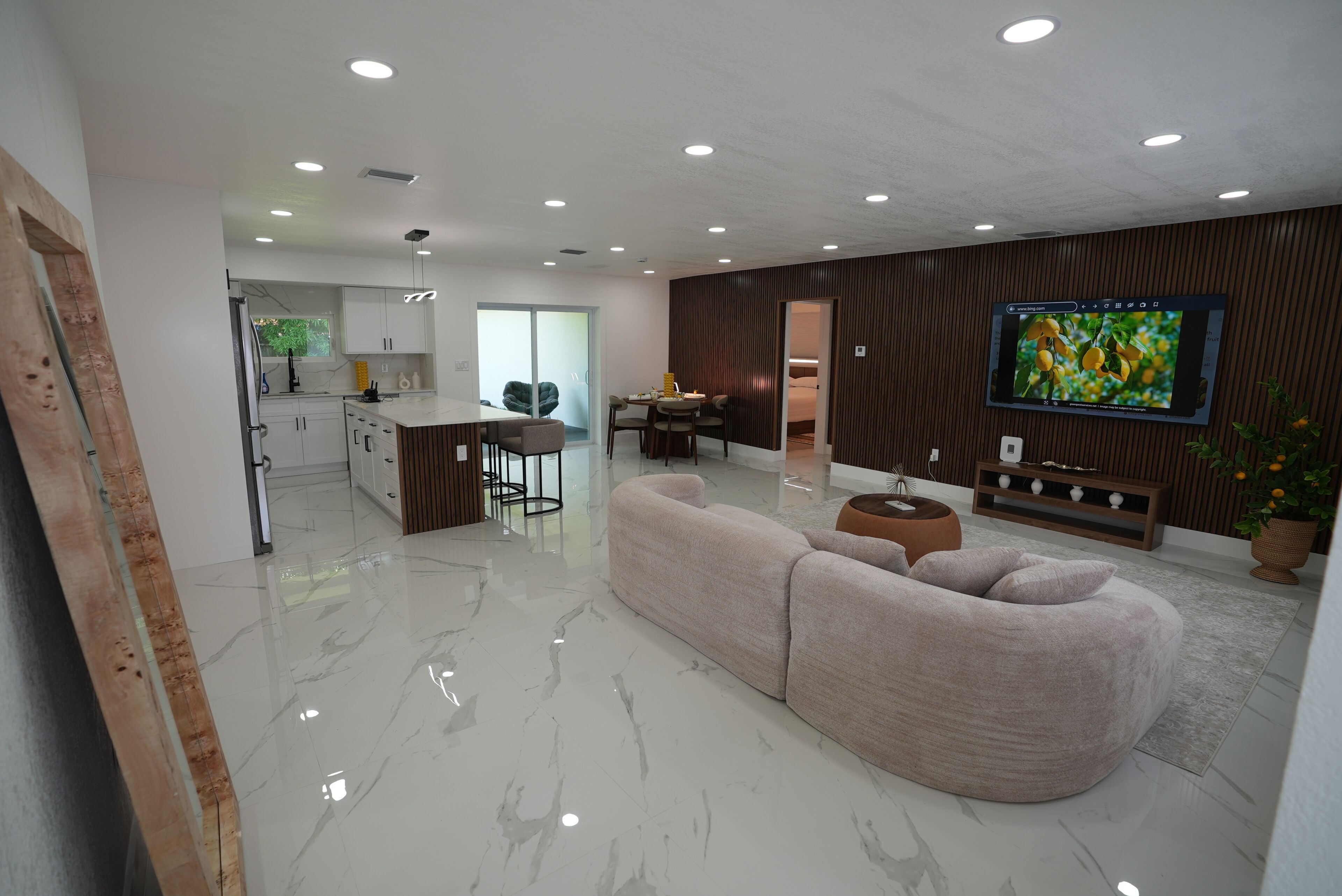 Una sala de estar moderna con un sofá grande, un comedor y una cocina con armarios blancos.
