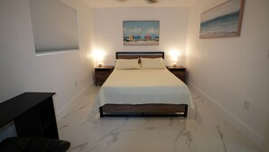 A bedroom with a bed, nightstands, a ceiling fan, a painting, and a window with blinds.