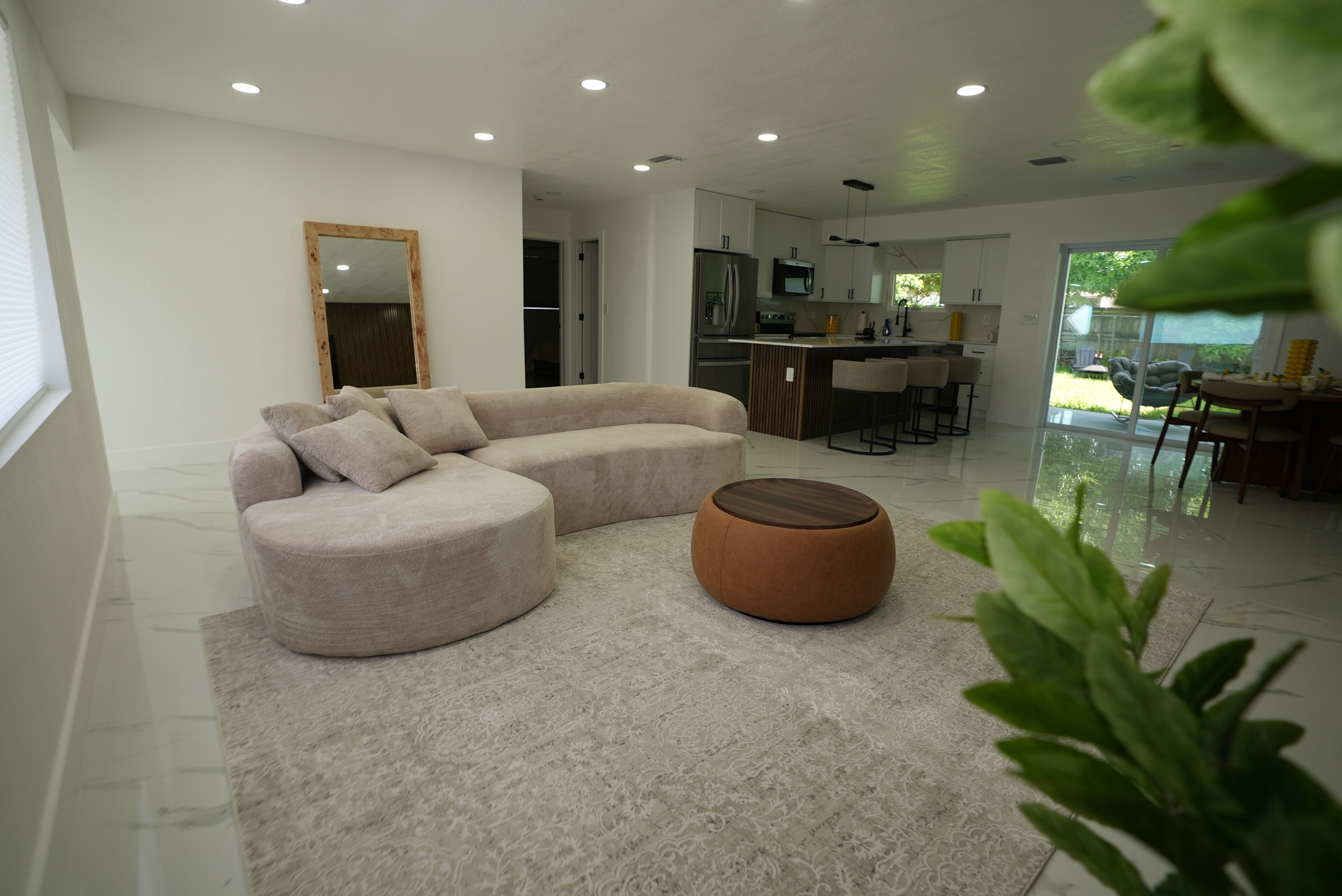 Una sala de estar moderna con un sofá modular, un reposapiés redondo y una cocina al fondo.