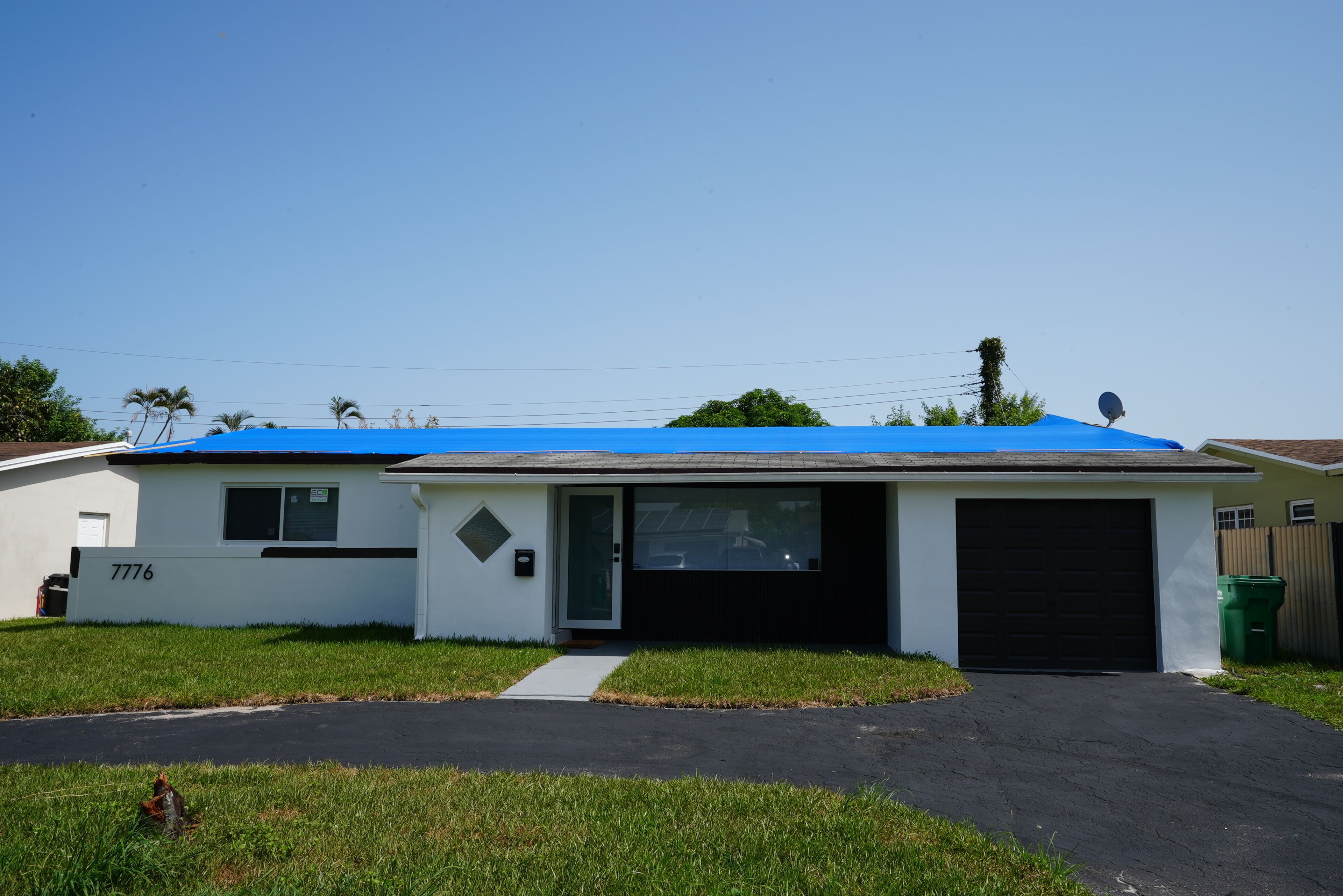 A single-story house with a garage, a blue roof, and a number '7776' on the side.