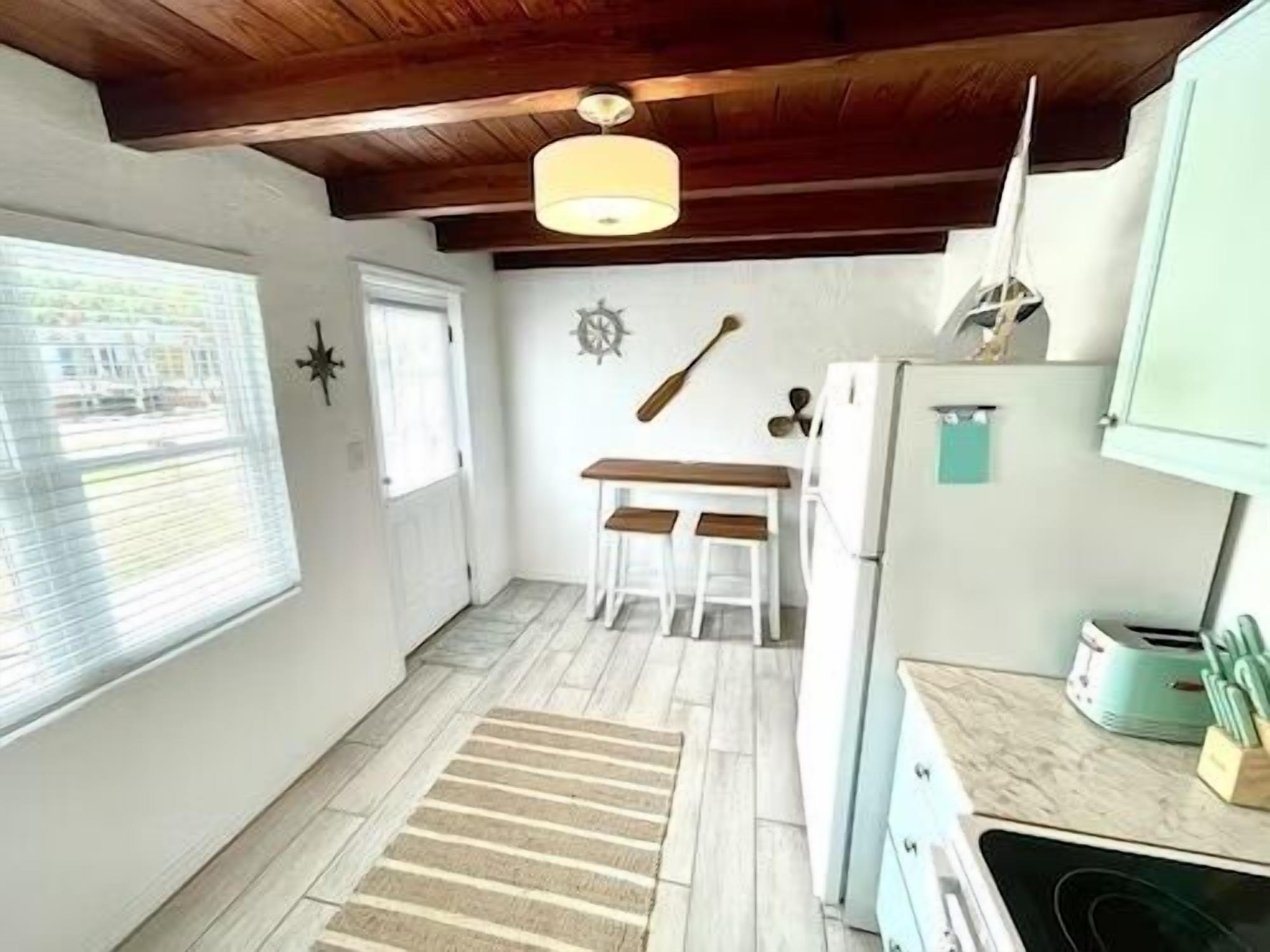Una cocina compacta con techo de madera, una mesa de comedor con dos sillas y un refrigerador.