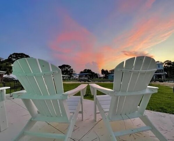 Two white Adirondack chairs facing a sunset with a clear sky. - Walk to Mashes Sands Beach, boat from your private dock, and bask in Old Florida in this one-story canal-front home (Panacea)