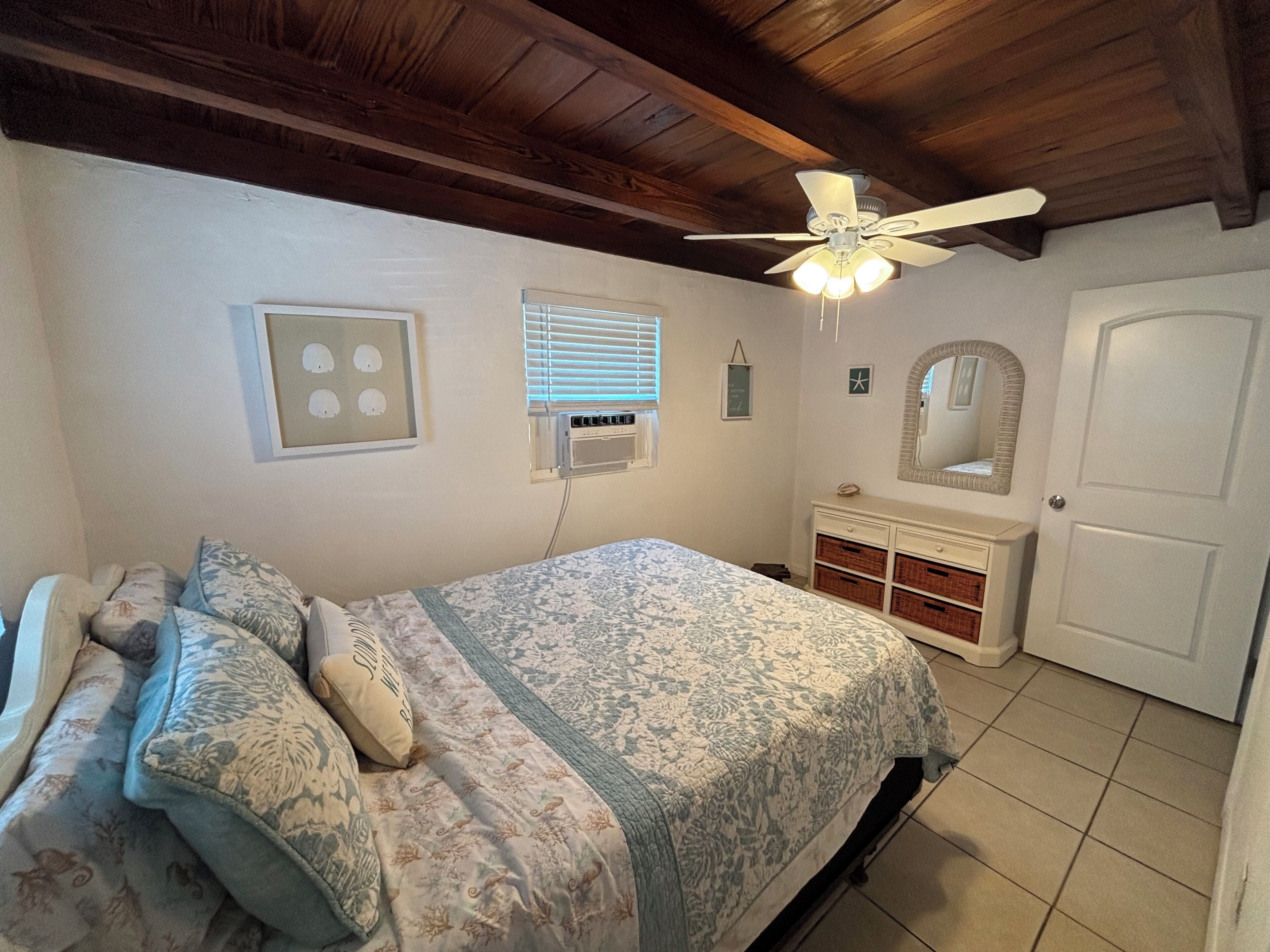A bedroom with a bed, dresser, ceiling fan, and a door.