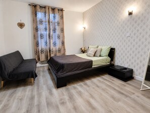 Un dormitorio con cama, sofá, mesita de noche y lámpara de pared.