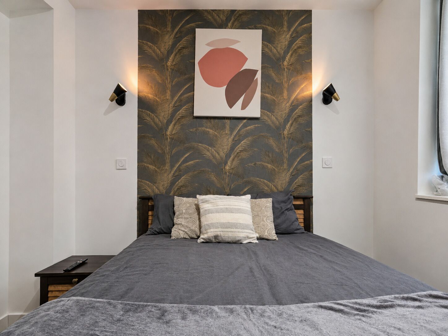 Ein Schlafzimmer mit einem Bett, einem Nachttisch, einer Wandleuchte und einem Wandbild.