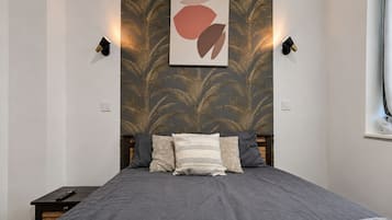 Een slaapkamer met een bed, nachtkastje, een wandlamp en een kunstwerk aan de muur.