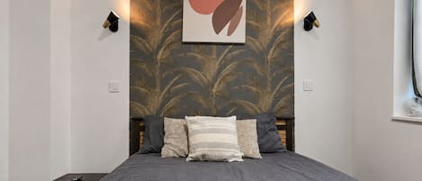 Une chambre à coucher comprenant un lit, une table de chevet, une lampe fixée au mur et une œuvre d’art décorative.