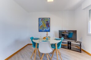 A dining area with a round table, blue chairs, a painting above the table, and a television on the wall. - FLOTS BLEUS AP4513 By Riviera Holiday Homes (Villefranche-sur-Mer)