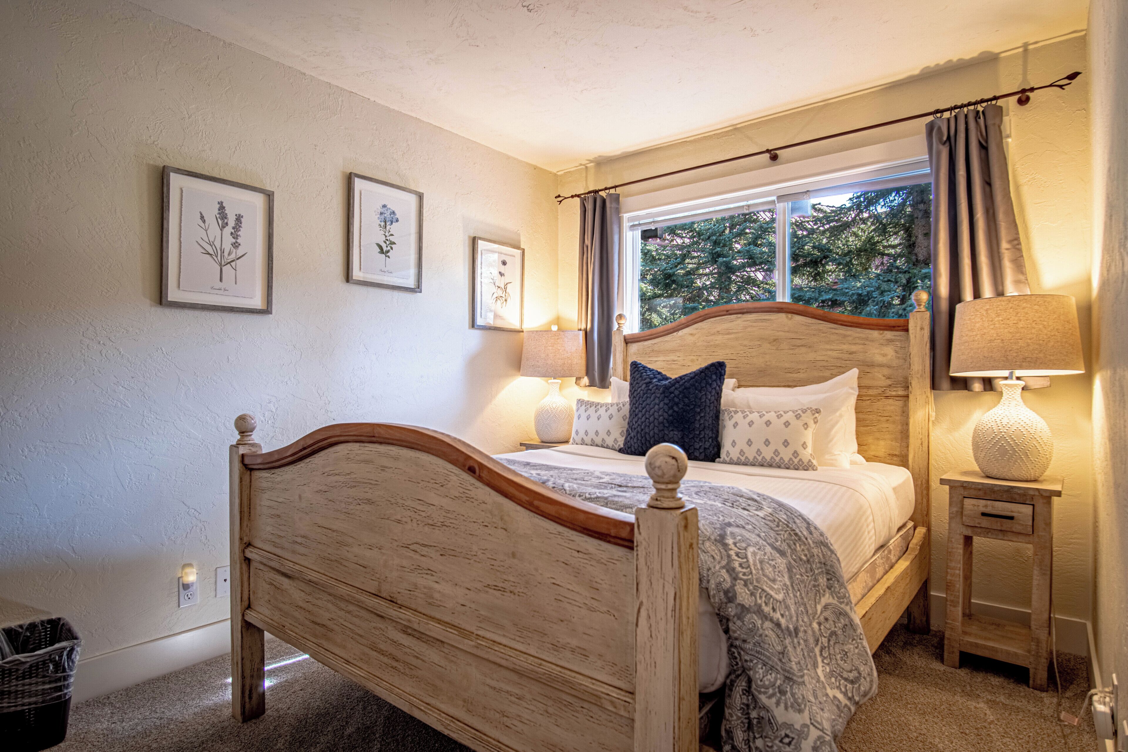 Un dormitorio con una cama de madera, una ventana con cortinas e impresiones botánicas enmarcadas en la pared.