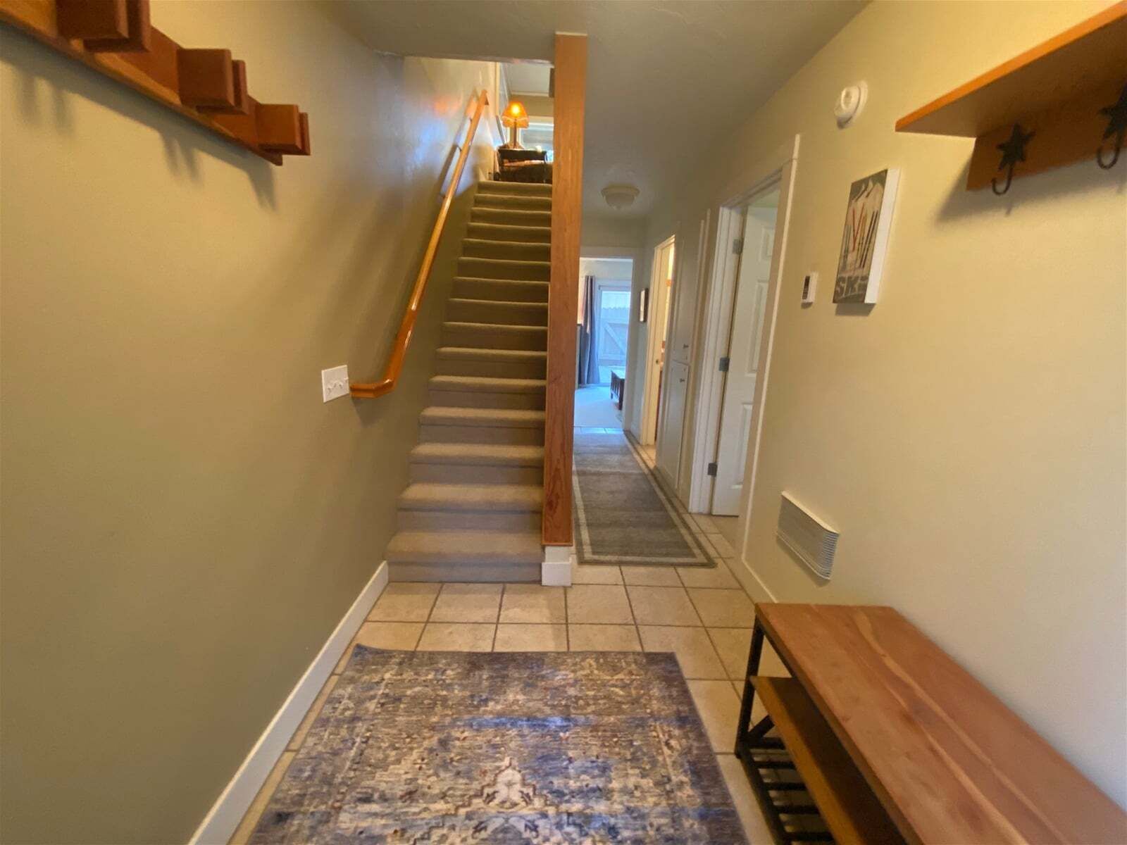 A hallway with a wooden staircase, a bench, and a patterned rug.