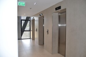 Ein Flur mit Wegweiser, zwei Aufzügen und einer Treppe mit Metallgitter.