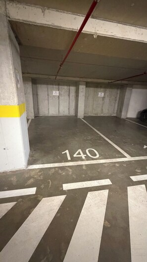 A parking garage with concrete walls, a yellow and white striped column, and a white line marked '140' on the floor. - Lake View Reaidenc (Tiranë)