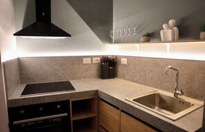 A modern kitchen with a built-in stove, a stainless steel sink, and a black range hood. - Lake View Reaidenc (Tiranë)