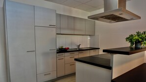 A modern kitchen with light-colored cabinets, a black countertop, and a stainless steel range hood.