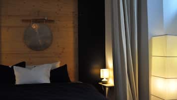 A bedroom with a wooden headboard, a round wall decoration, a bed with pillows, a bedside table with a lamp, and a curtain.