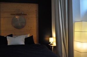Ein Schlafzimmer mit Holz-Kopfteil, einer runden Wanddekoration, einem Bett mit Kissen, einem Nachttisch mit Lampe und einem Vorhang.