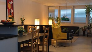 A modern living room with a dining area, featuring a sofa, chairs, a table, and potted plants.