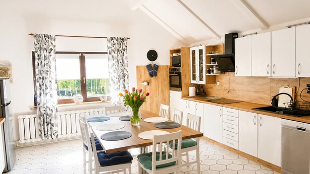 A modern kitchen with white cabinets, a wooden countertop, and a dining area with a table set for four. - Holiday Home for 8 People Mrzezyno (Trzebiatow)
