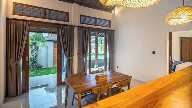 Un coin repas avec une table et des chaises en bois, un ventilateur de plafond et un luminaire en matière tressée.