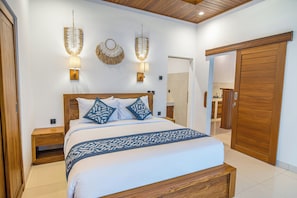 Un dormitorio con estructura de cama de madera, ropa de cama blanca y apliques decorativos.