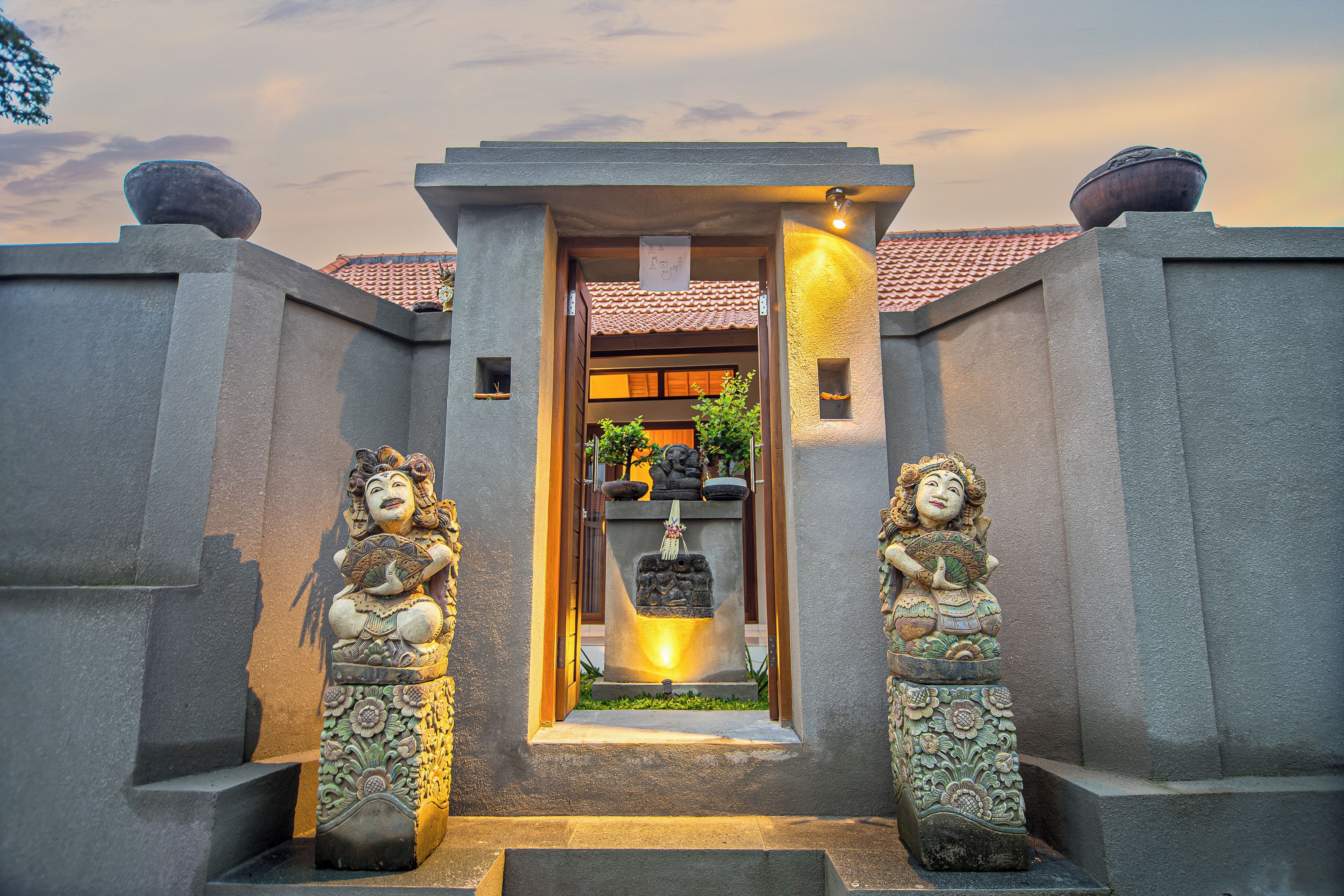 A traditional entrance with a central door, flanked by two statues, leading to a building with a tiled roof.