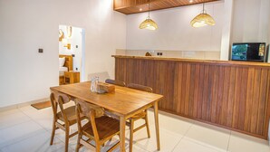 Une table à manger en bois avec des chaises, un coin cuisine doté d’un comptoir en bois et des luminaires suspendus.