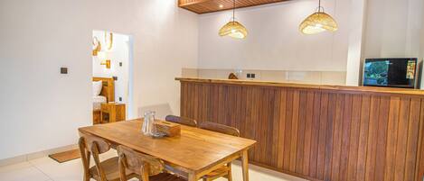 A wooden dining table with chairs, a kitchen area with a wooden counter, and pendant lights.