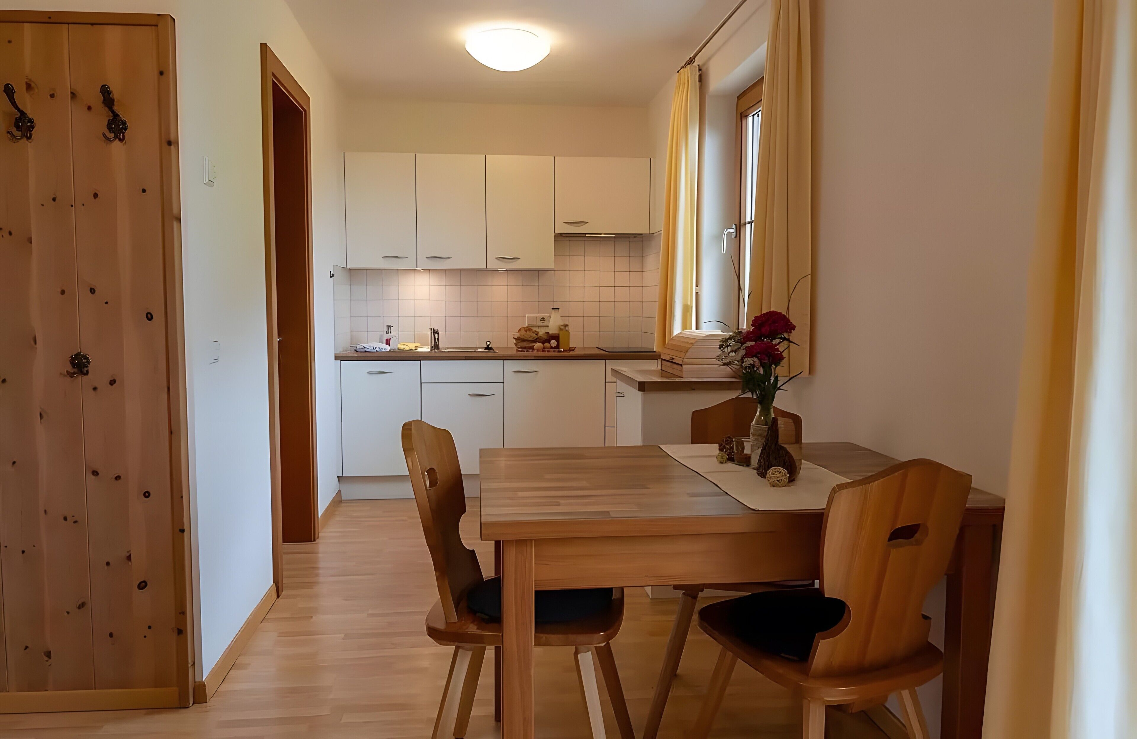 A compact kitchen with white cabinets, a wooden dining table, and chairs.