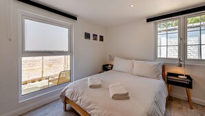 Ein Schlafzimmer mit einem Bett, zwei Nachttischen, einem Fenster mit Blick auf eine Außenanlage.
