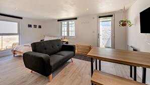 Ein modernes Schlafzimmer mit einem Bett, einem dunkelgrauen Sofa, einem Holzesstisch und einem an der Wand befestigten Fernseher.