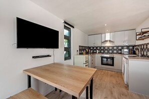 A modern kitchen with a flat-screen TV mounted on the wall, a built-in oven, and a microwave. - Host & Stay | Studio 58 (Brighton and Hove)