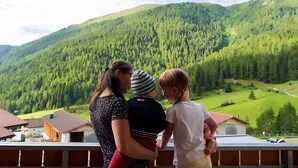 Eine Familie auf einem Balkon mit Blick auf eine gebirgige Landschaft und dichte Wälder.