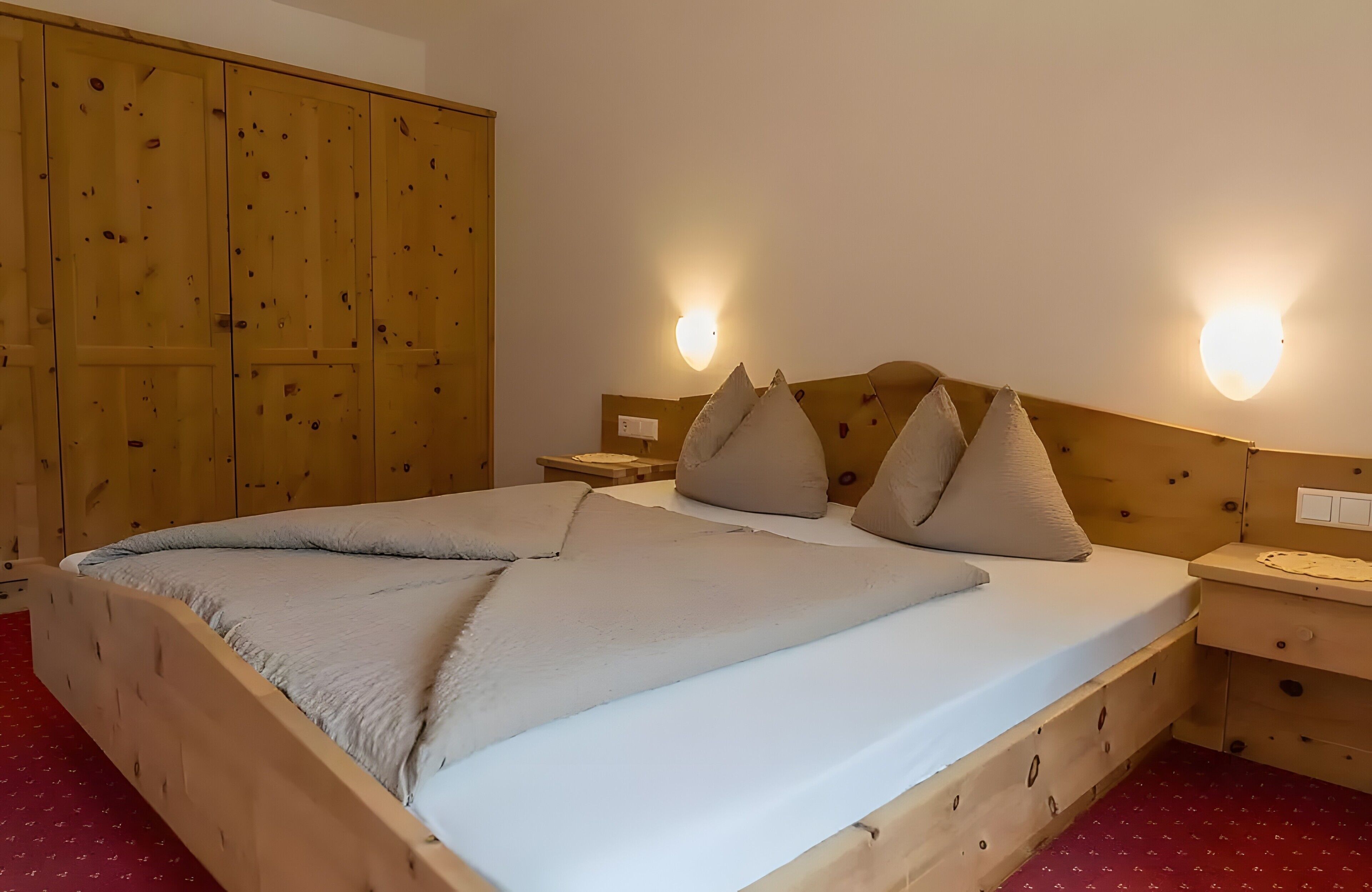 Un lit en bois avec un matelas blanc et des oreillers beige, une armoire en bois et deux lampes fixées au mur.