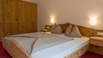 Un lit en bois avec un matelas blanc et des oreillers beige, une armoire en bois et deux lampes fixées au mur.