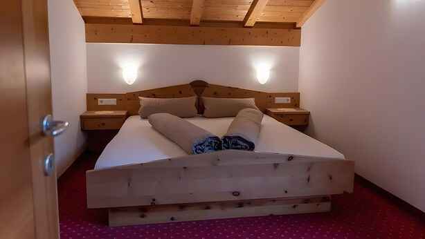 Ein hölzernes Bett mit Kopfteilen, zwei Nachttische und ein roter Teppich mit Muster.