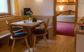 A wooden dining table with chairs, a vase with flowers, and a bench in a room with a bunk bed in the background. - Apartment "Watles" with Balcony and Wi-Fi (Mals)