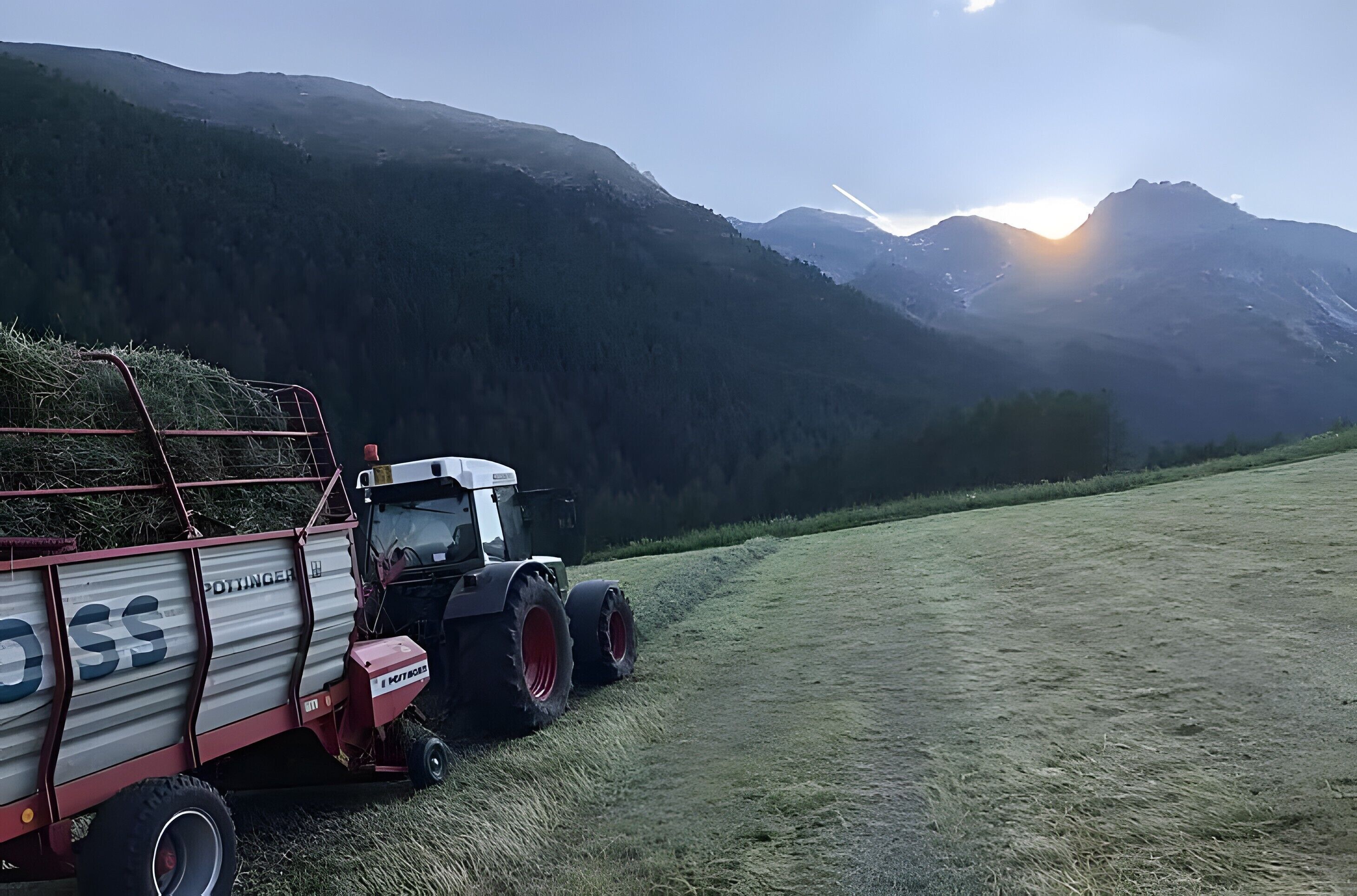 A tractor with a trailer in a field with mountains in the background.