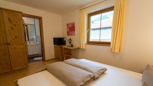 Ein Schlafzimmer mit einem Bett, einem Schreibtisch mit Stuhl, einem Fernseher und einem Fenster mit Vorhängen.